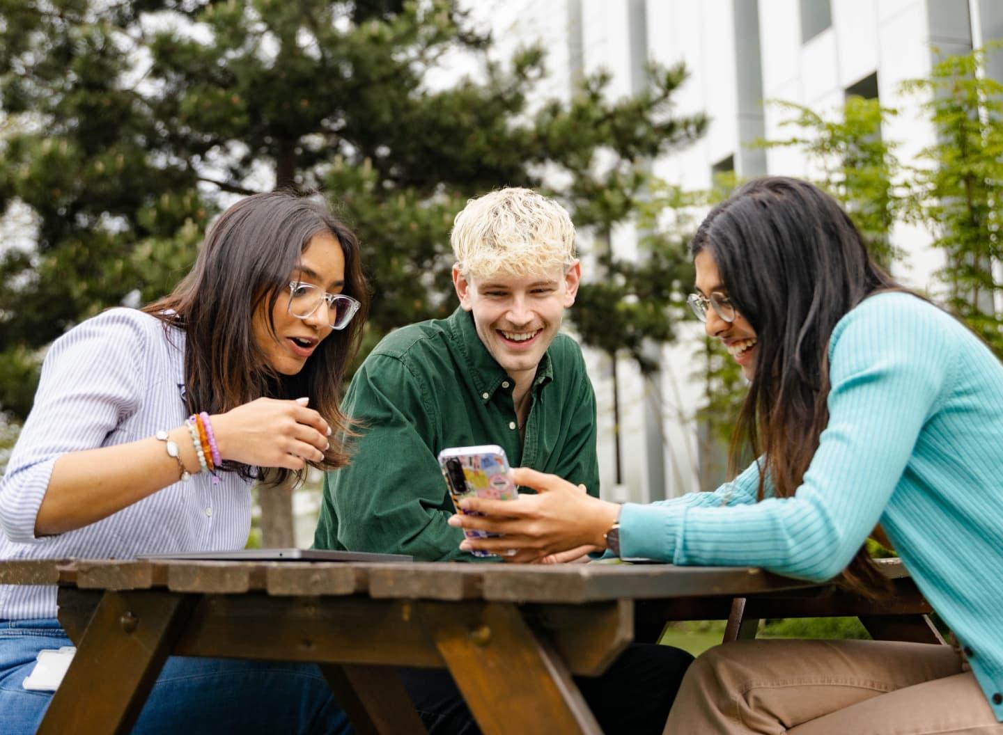 group of people look at a phone screen on a outdoor bench