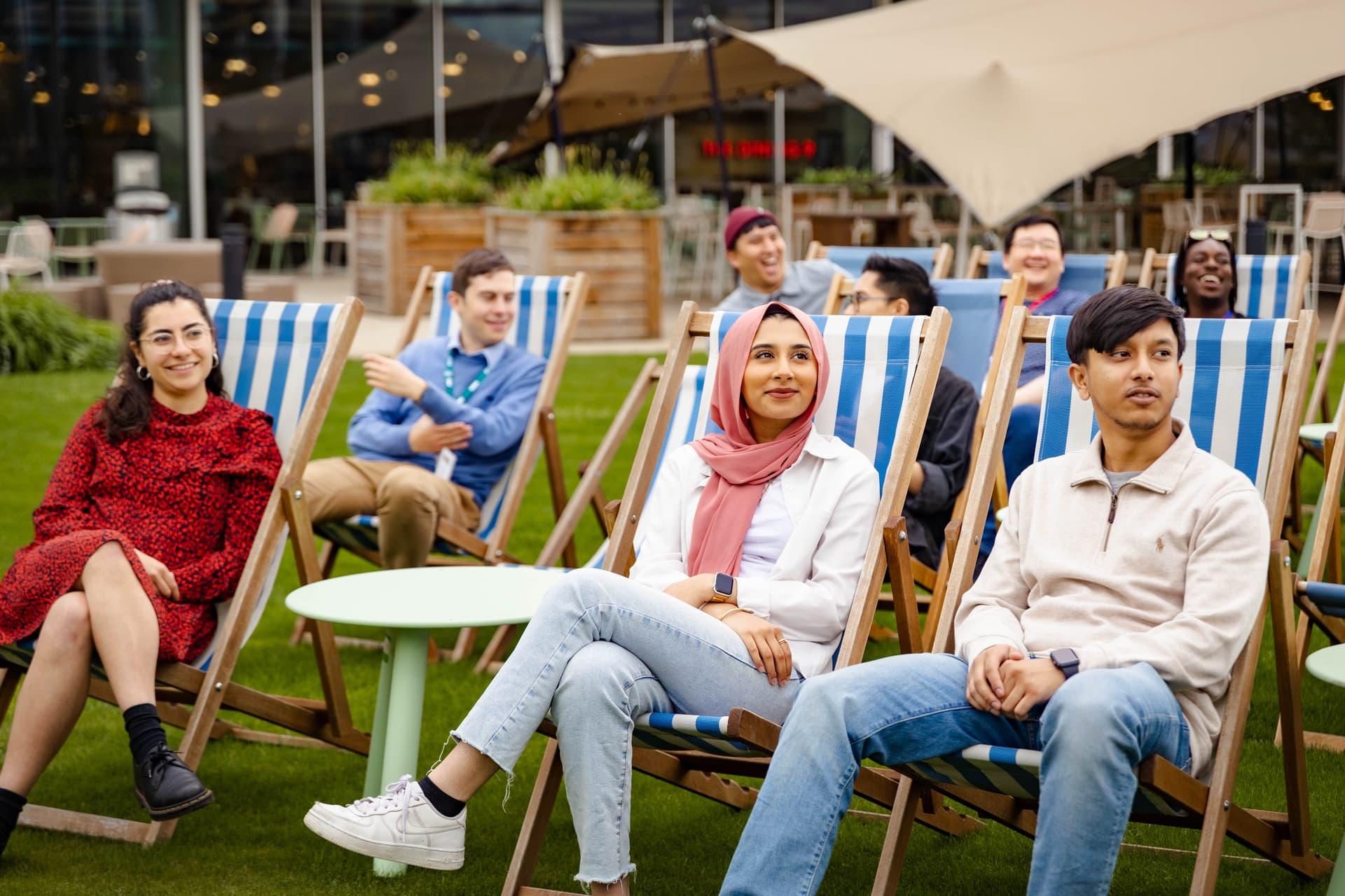 A group of people sitting on striped deckchairs, smiling and looking at someone in the distance