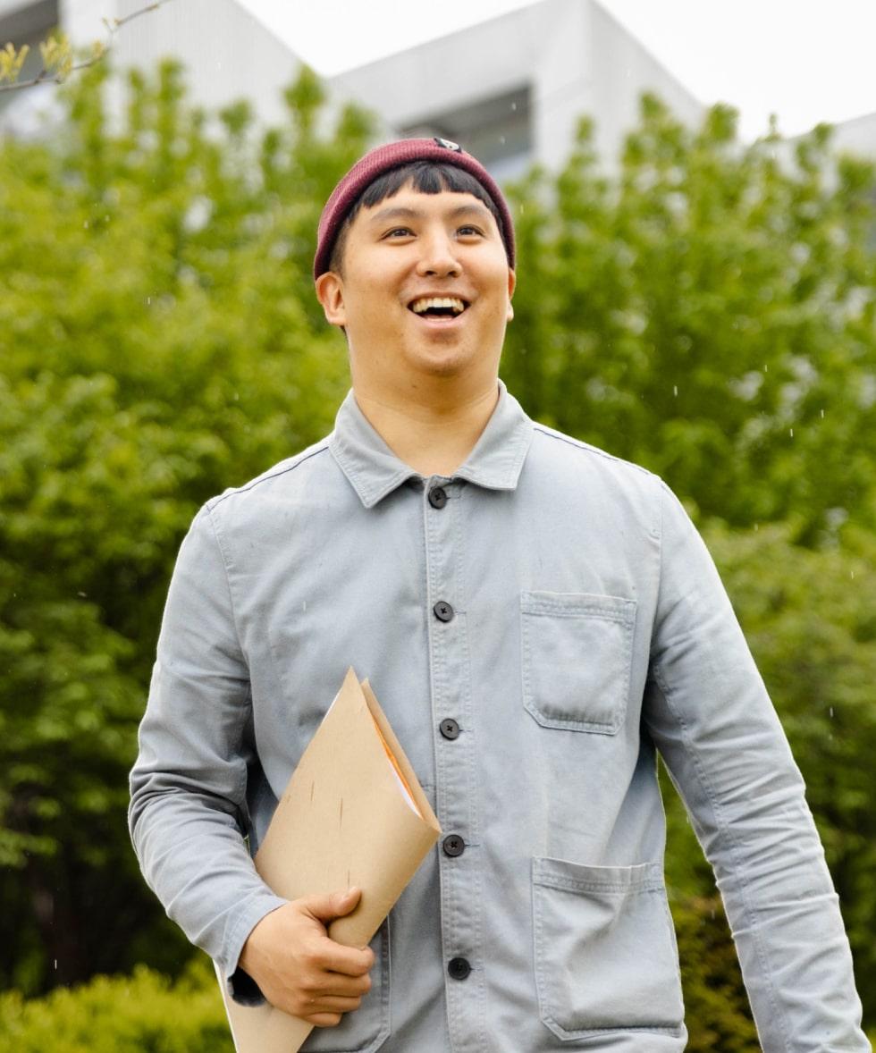 Man smiling outdoors holding a folder