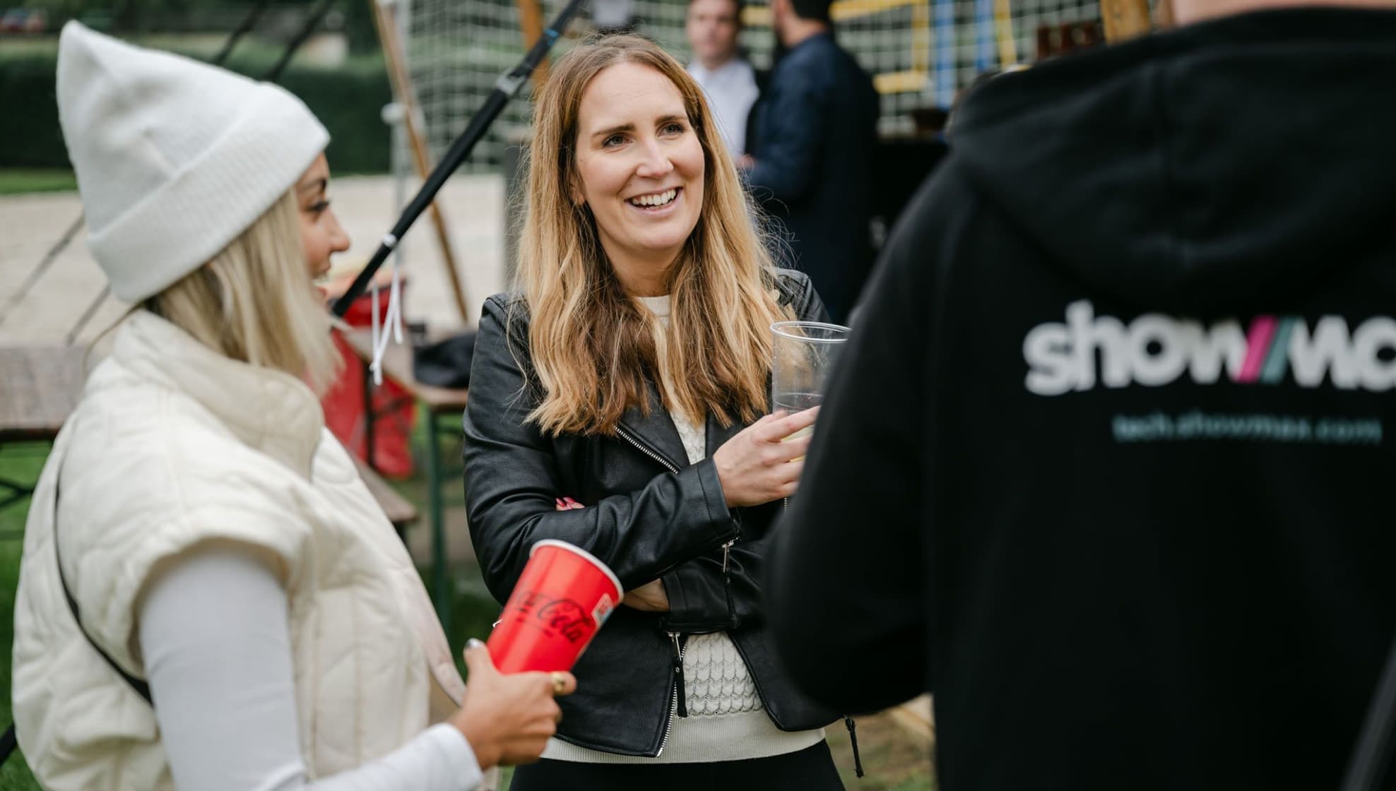 Three colleagues chatting outdoors with drinks, one in a Showmax hoodie.