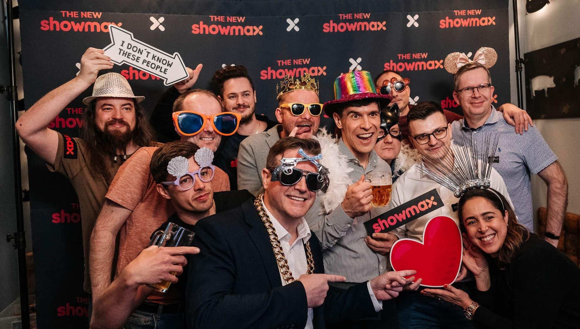 Group in fun costumes posing together at a Showmax event, holding props and drinks.