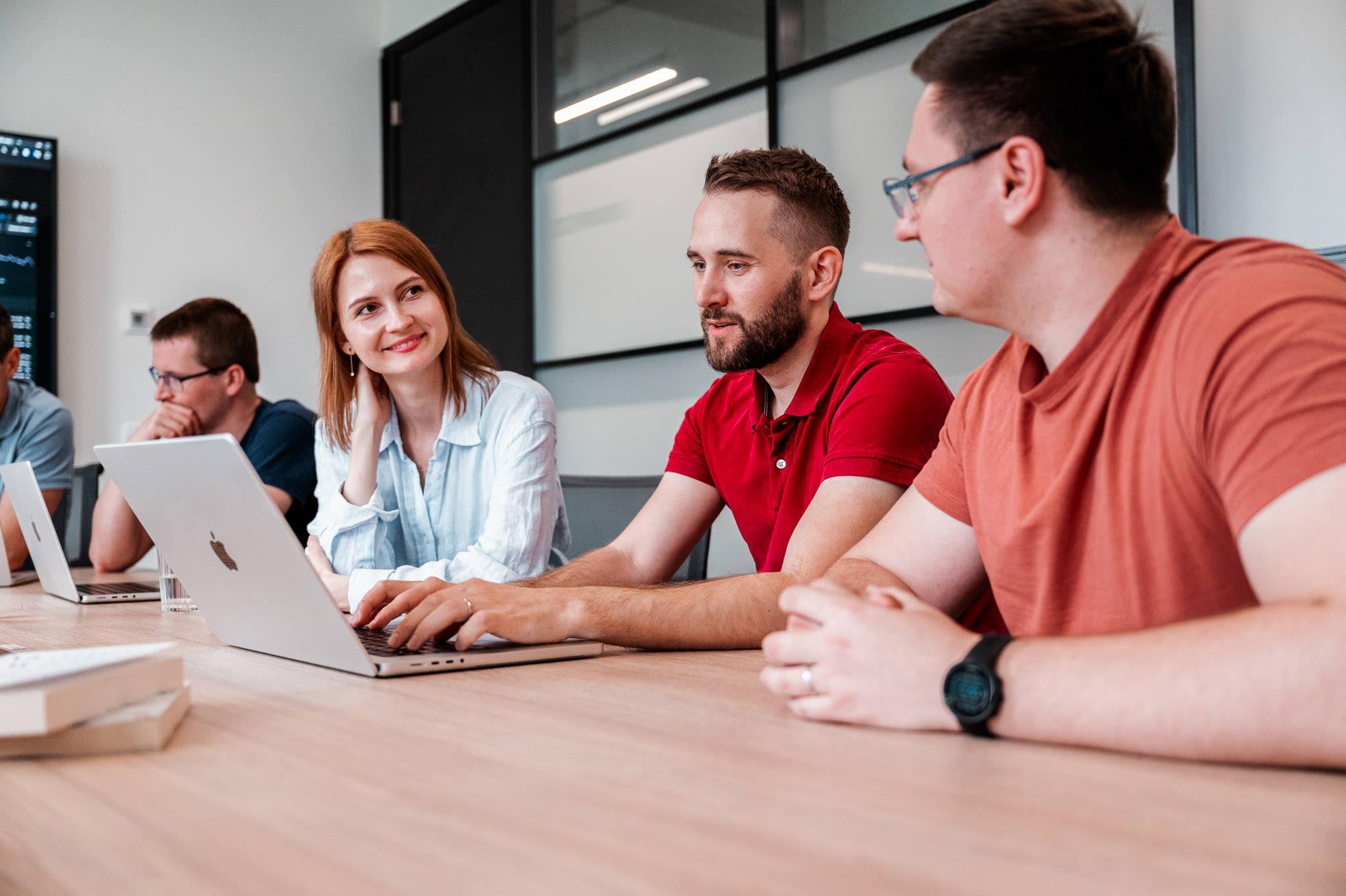 Team seated at a table with laptops, discussing in a bright meeting room.
