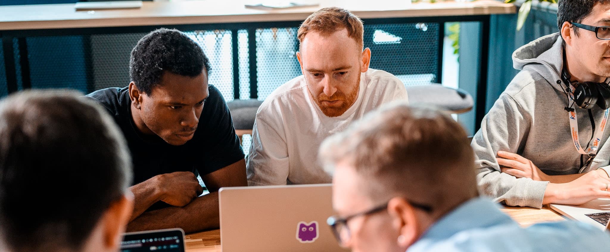 Five people gathered around a desk, focused on laptops during a collaborative work session.