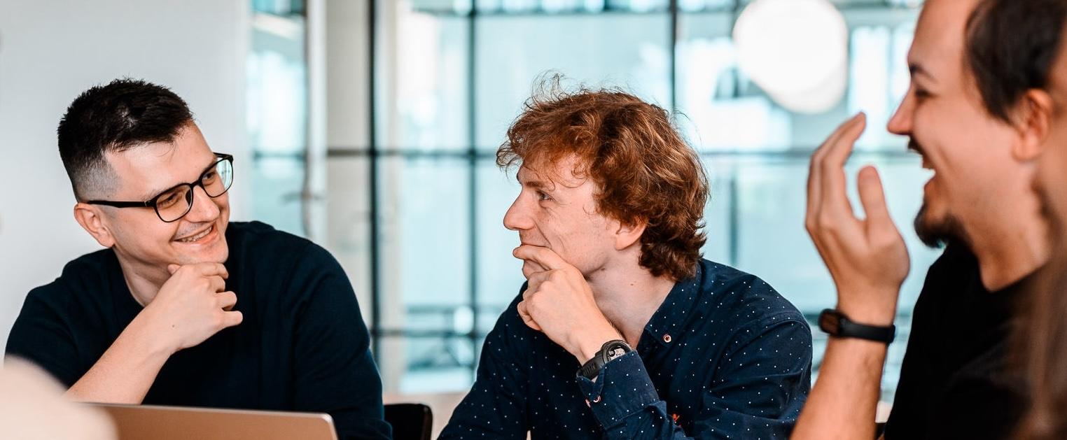 Group of colleagues laughing and chatting around a table in a bright modern office.