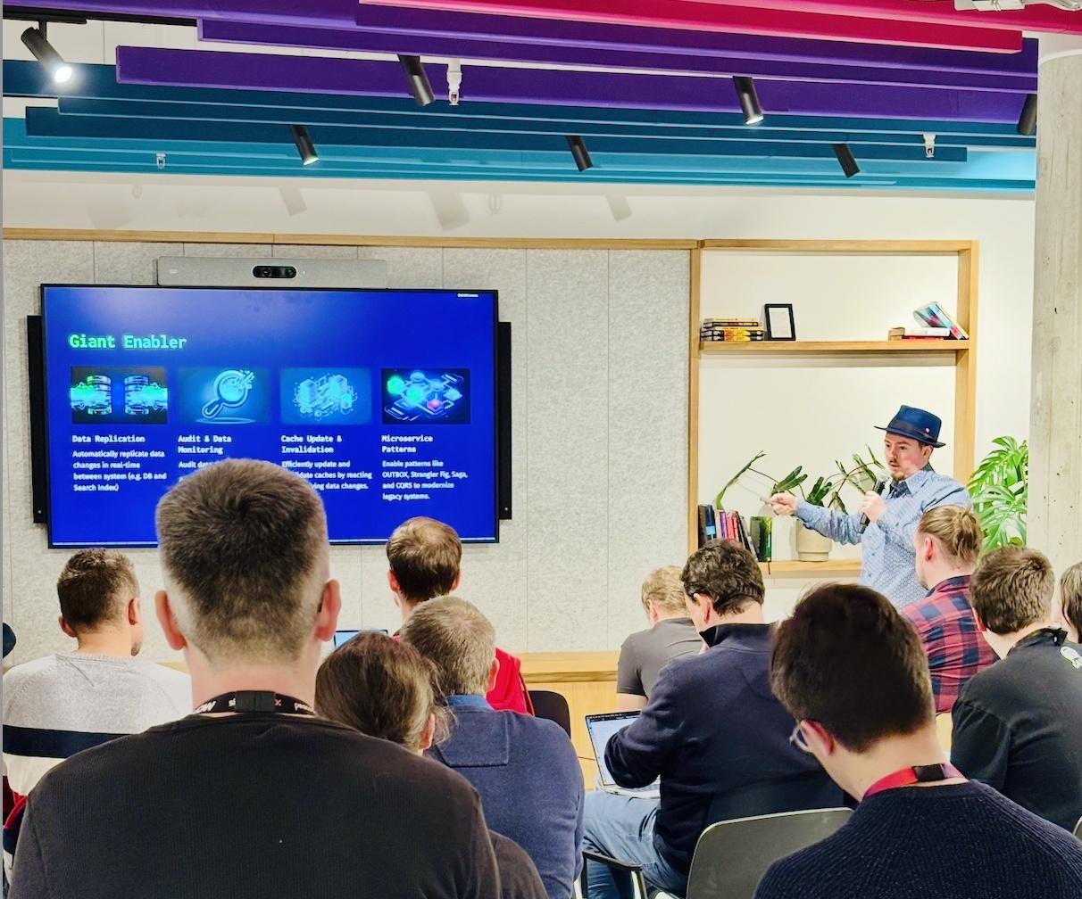 Man in a hat giving a tech talk with a mic, presenting to a seated audience in front of a screen labeled “Giant Enabler.”