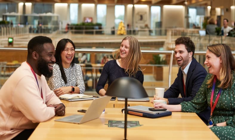 group of people working together at a desk and laughing