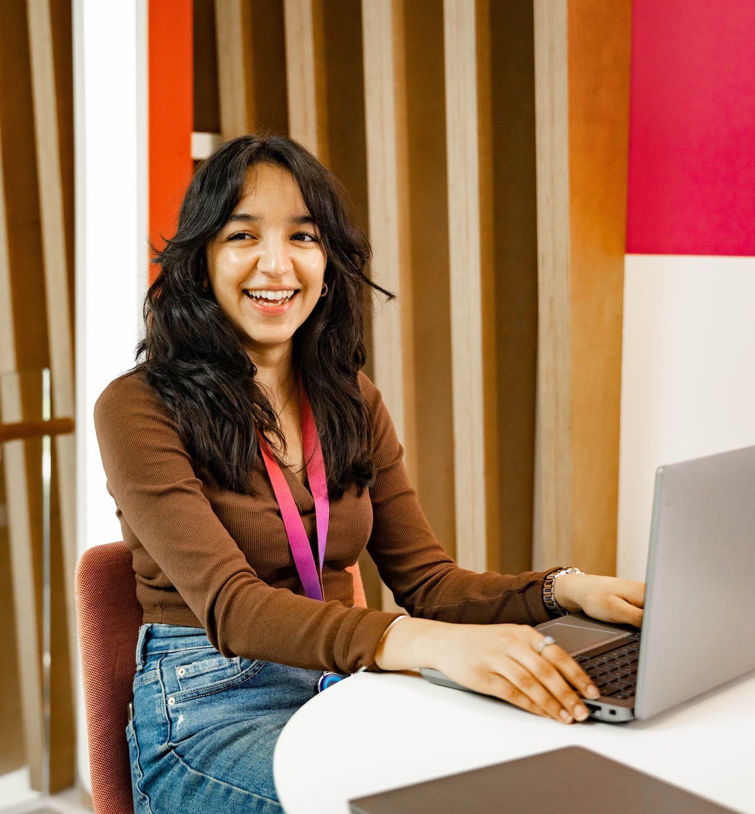 Smiling woman seated at a round desk using a laptop in a Sky office with wood-panel walls.