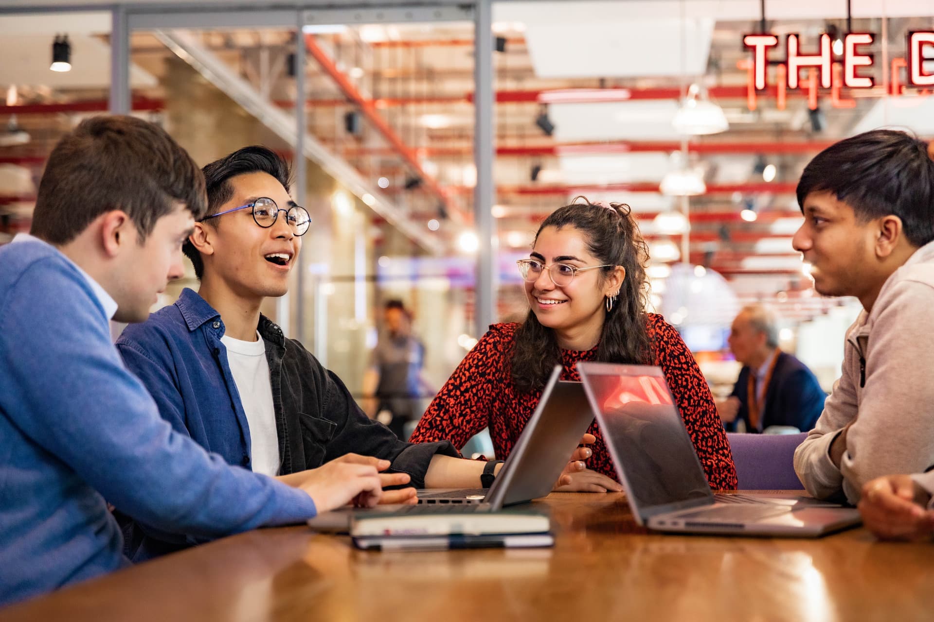 Group of young professionals talk around a table with laptops in a vibrant Sky office space.