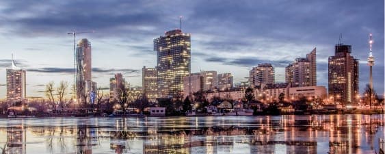 Stadtansicht in der Abenddämmerung, Gebäude spiegeln sich im ruhigen Wasser unter einem bewölkten Himmel.