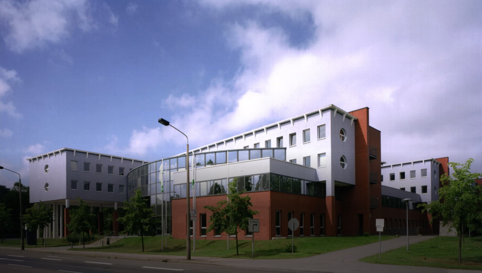 Ein großes, modernes Sky-Bürogebäude mit weißen und roten Backsteinteilen, Glasfassade und Bäumen am Straßenrand.
