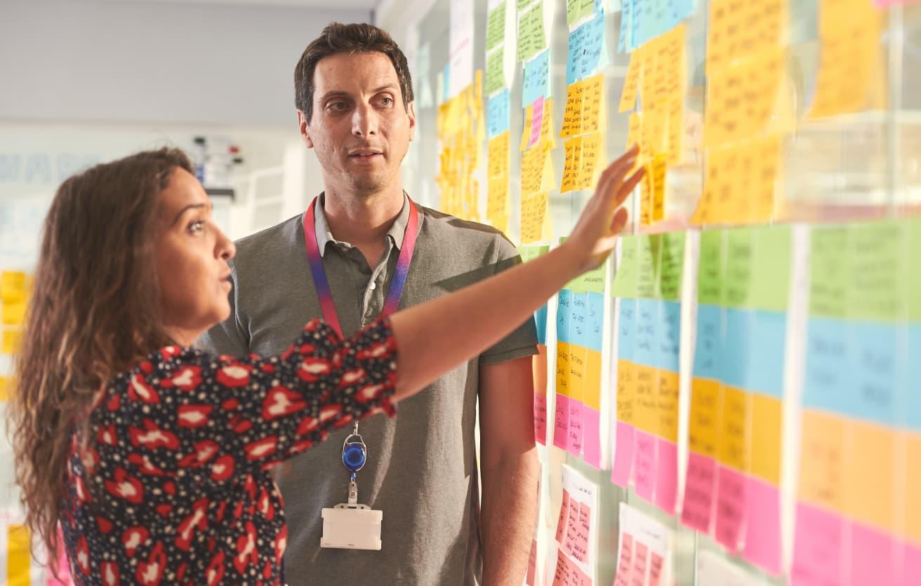a woman and a man looking at sticky notes on a transparent wall