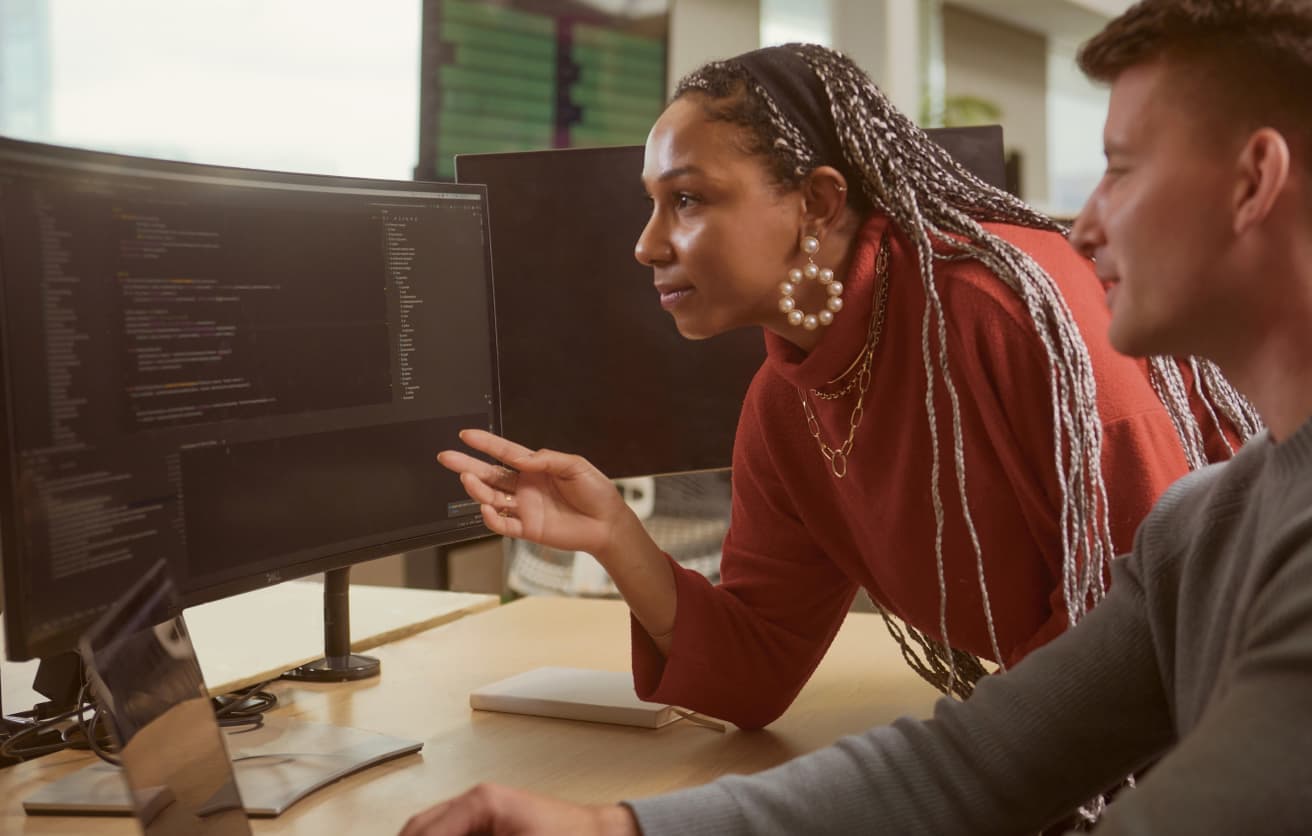 man sitting at a desk with woman leaning over analysing the monitor screen