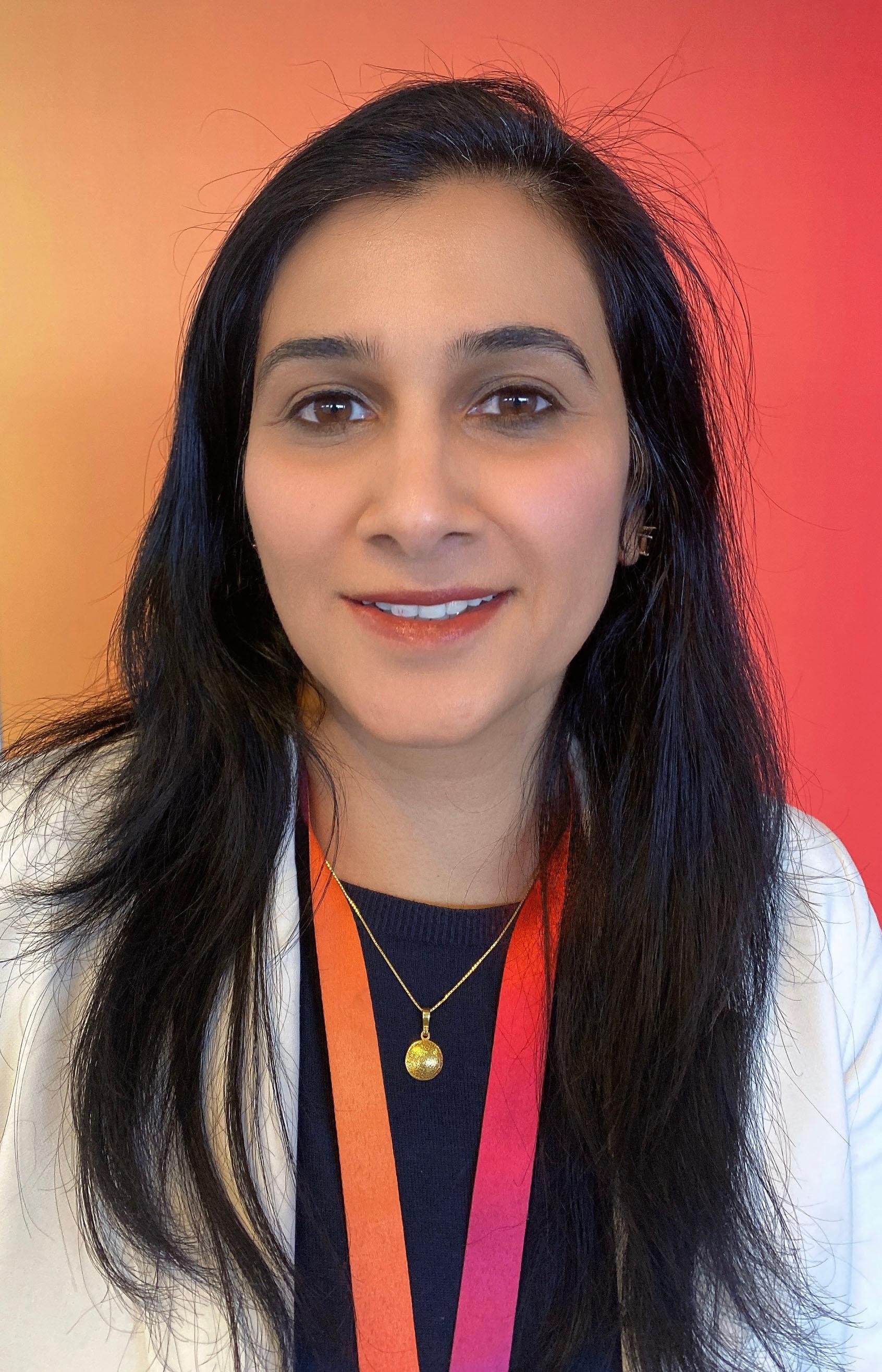 Sujata standing in front of a spectrum red-orange well, wearing a similar coloured Sky lanyard around her neck.