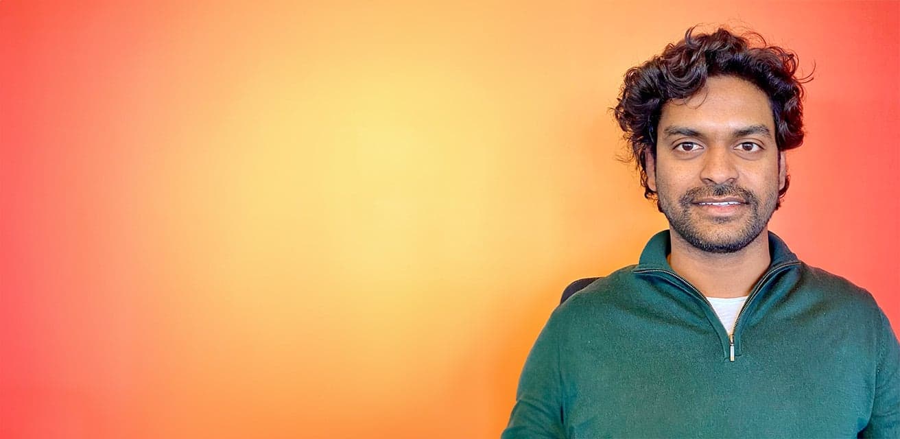 Man in a green zip-up top smiling in front of a gradient orange and red background.