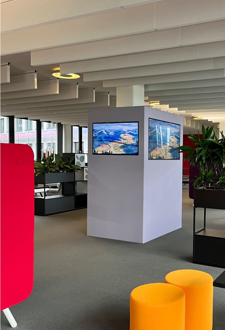 Sky office space with yellow stools, indoor plants, and screens showing scenic landscapes.