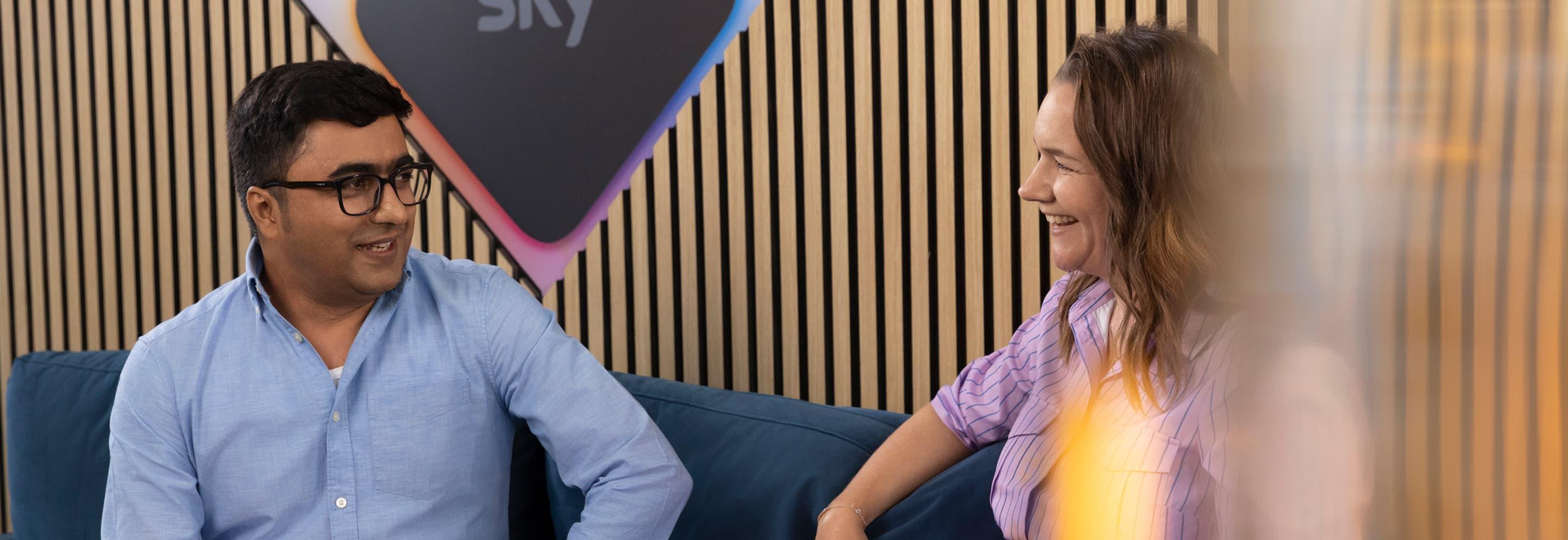 a man with glasses and a woman speaking on a sofa