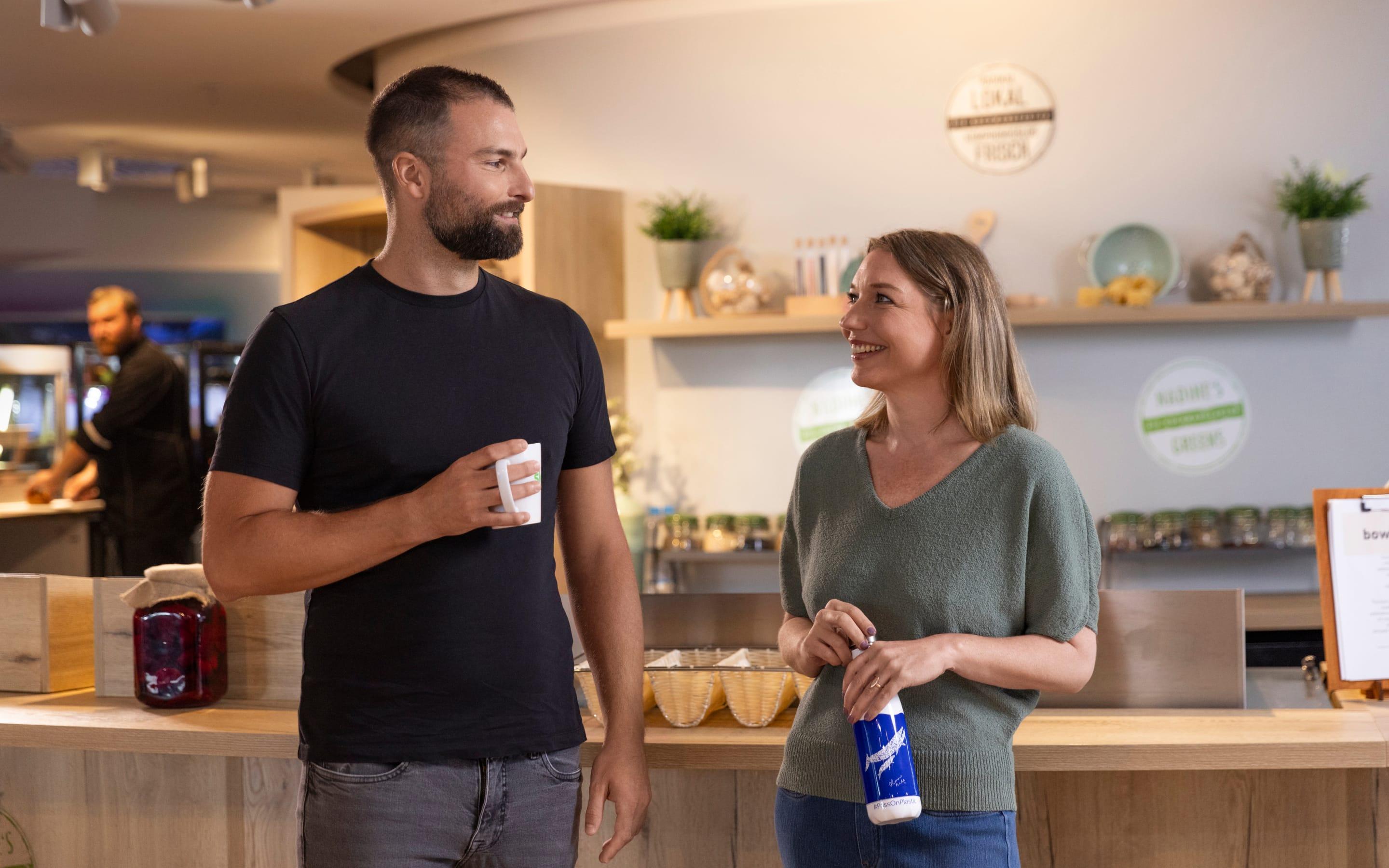 Two coworkers chat in a Sky office kitchen area, holding reusable mugs and bottles.