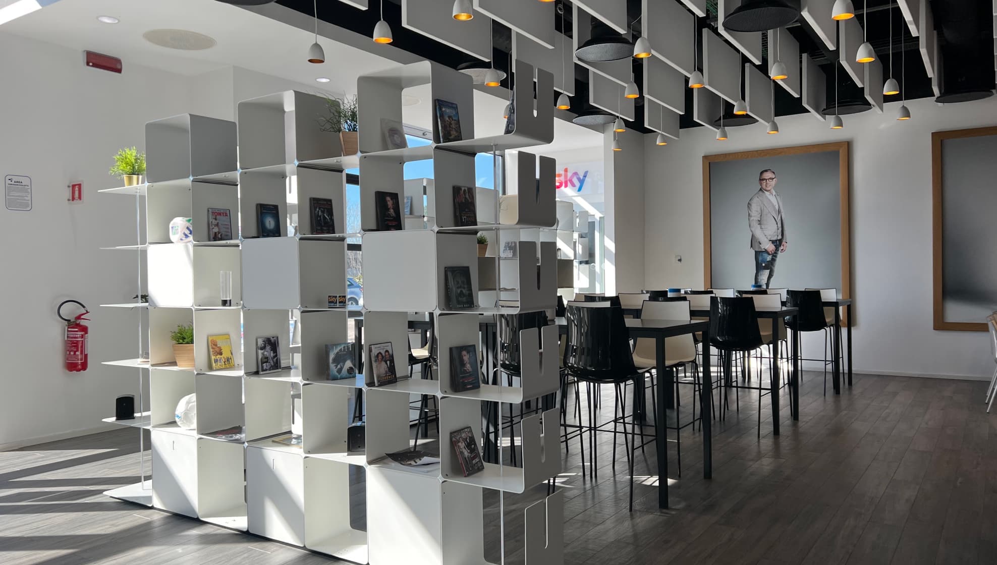 Luminosa zona lounge con librerie, tavoli alti, illuminazione moderna e un grande ritratto dello chef Bruno Barbieri sulla parete.