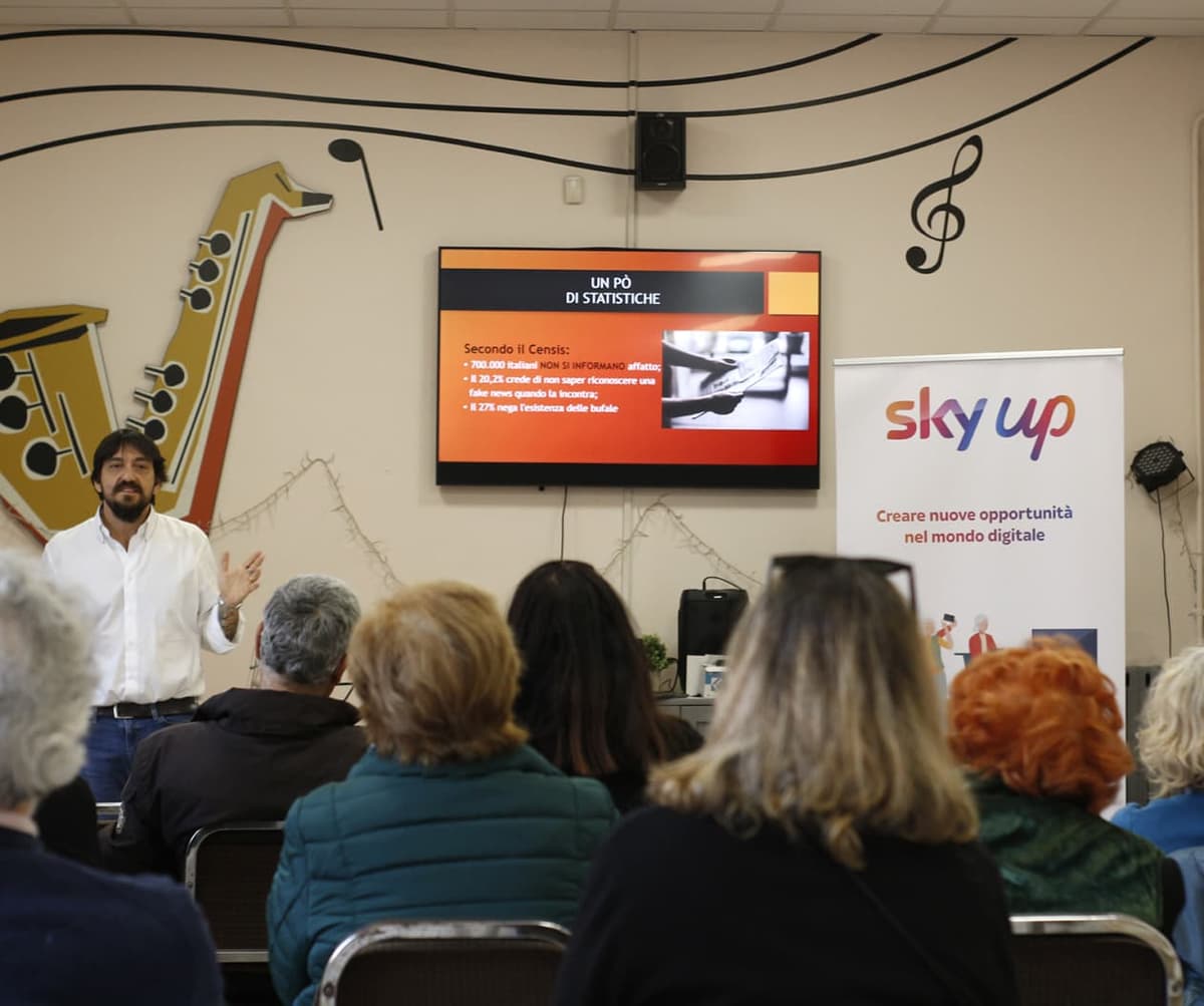 Man presents to a group with a screen showing statistics and a “Sky Up” banner about digital opportunities nearby.