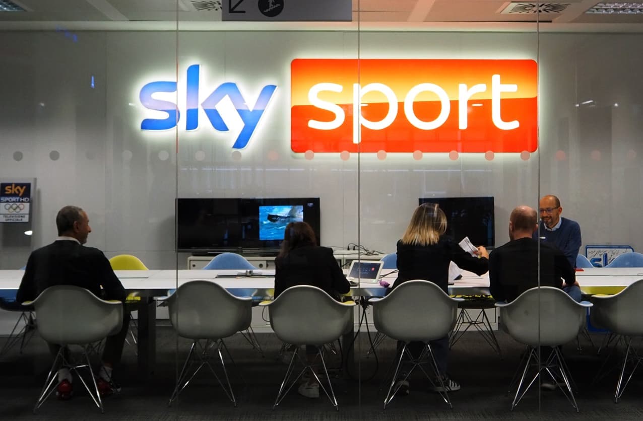 Group meeting in a glass-walled room with a large illuminated Sky Sport logo on the wall.