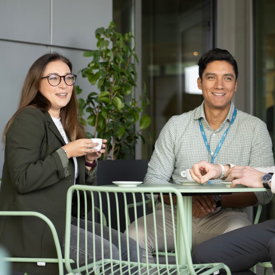 Two Sky employees smiling and chatting near a plant in a modern office setting, all wearing Sky lanyards